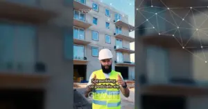 Pracownik GRANIT S.A. w kasku i kamizelce omawia postęp budowy budynku Henry Hudson na tle elewacji.